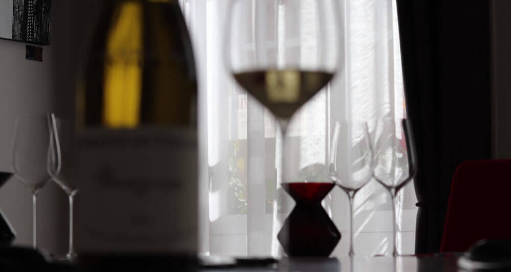 Intérieur lumineux d'une salle de dégustation à Beaune : bouteille floue au premier plan, verres prêts pour un cours d'oenologie.