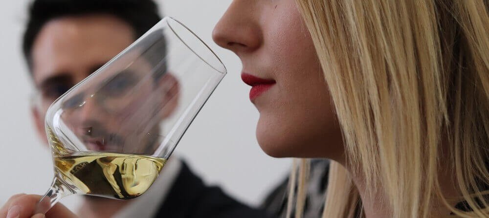 Gros plan d'une femme analysant les arômes d'un verre de vin blanc lors d'un cours d'oenologie structuré.