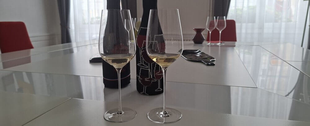 Deux verres de vin blanc sur une table de dégustation avec bouteilles masquées pour un cours d'oenologie à l'aveugle.